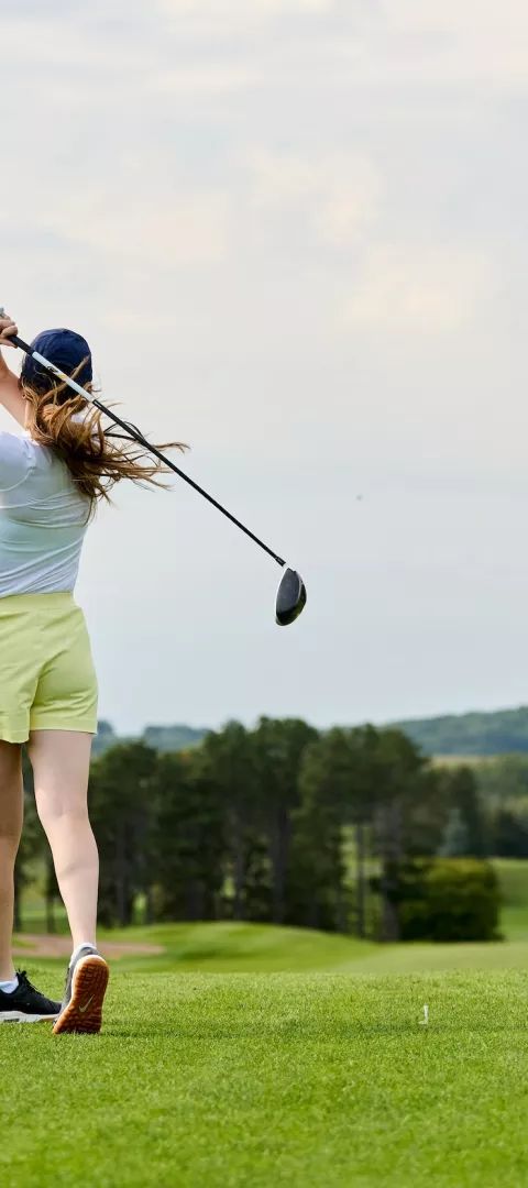 A woman swings a golf club at Baker National Golf Course